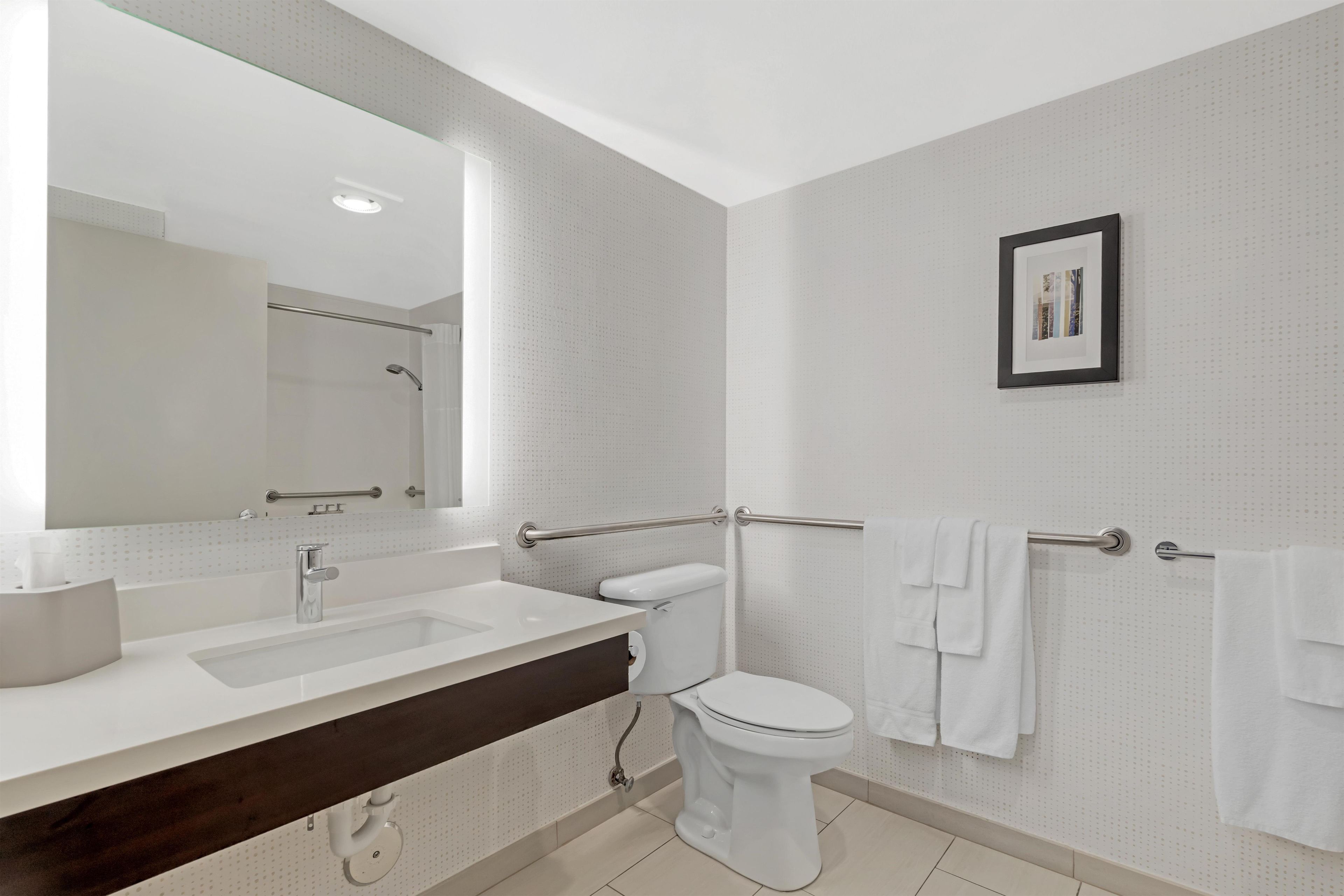A modern bathroom with a large mirror, a sink, a toilet, and a shower area.