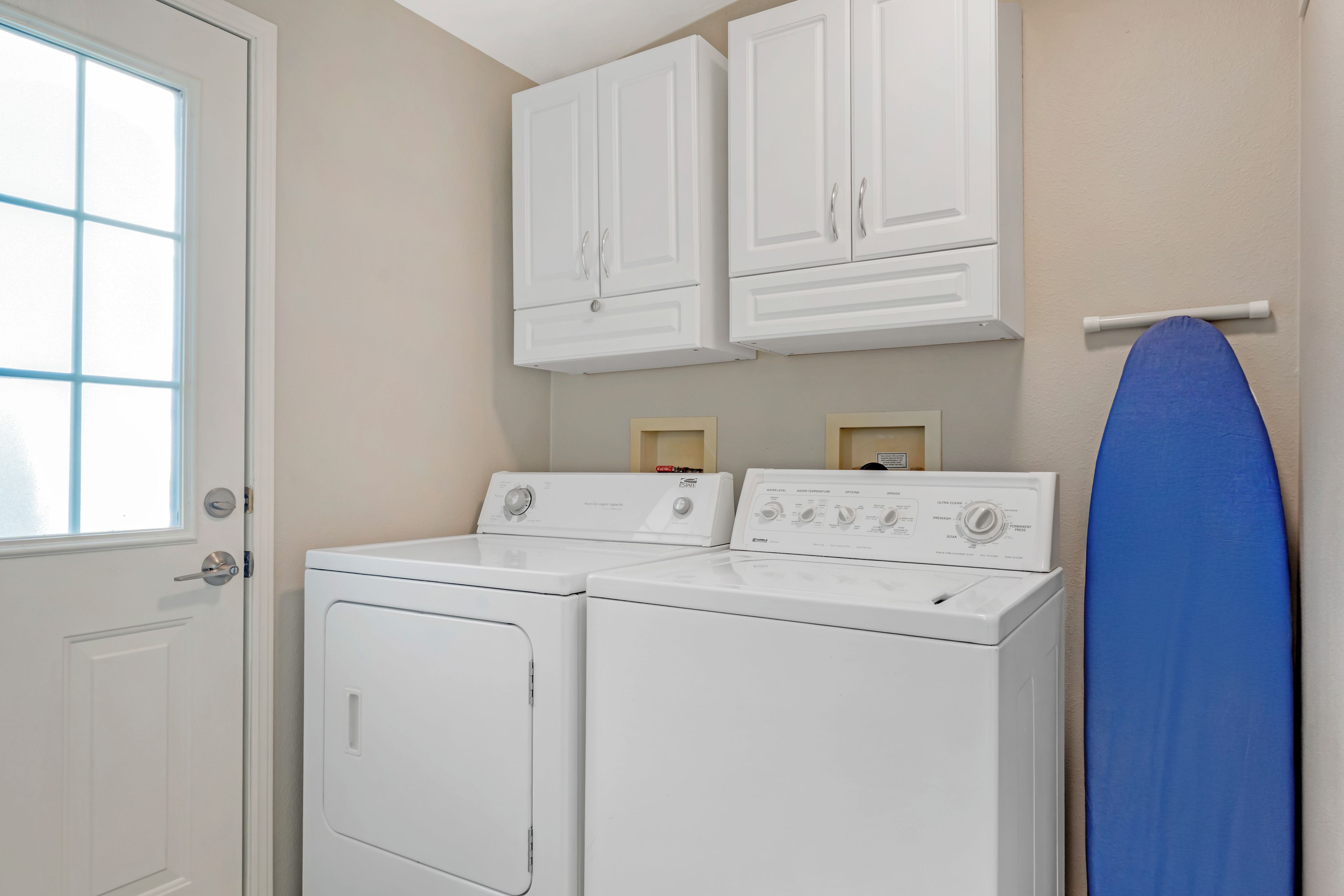 A laundry room with two white front-loading washing machines, a white door, and a towel rack with a blue towel.