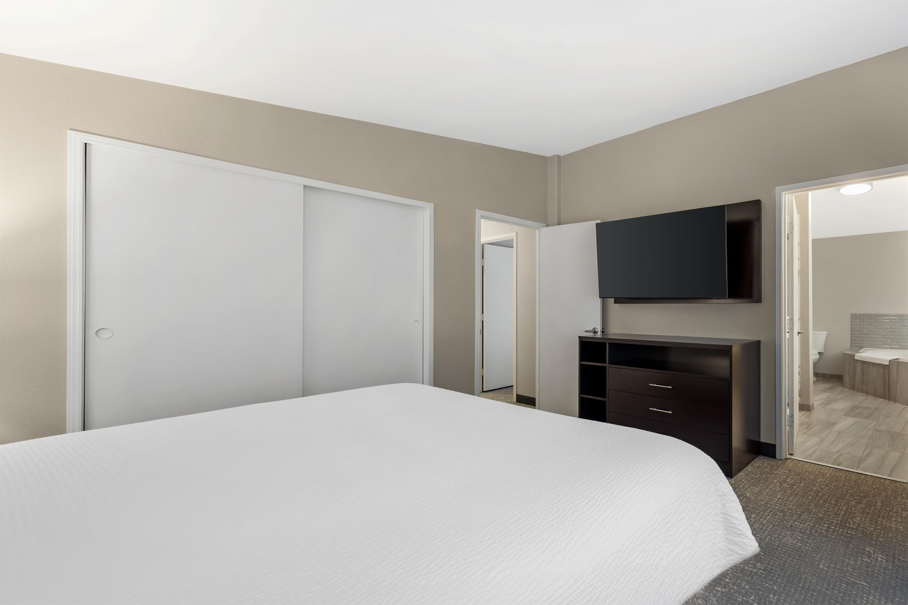 A bedroom with a bed, a dresser, a mirror, and a door leading to a bathroom.