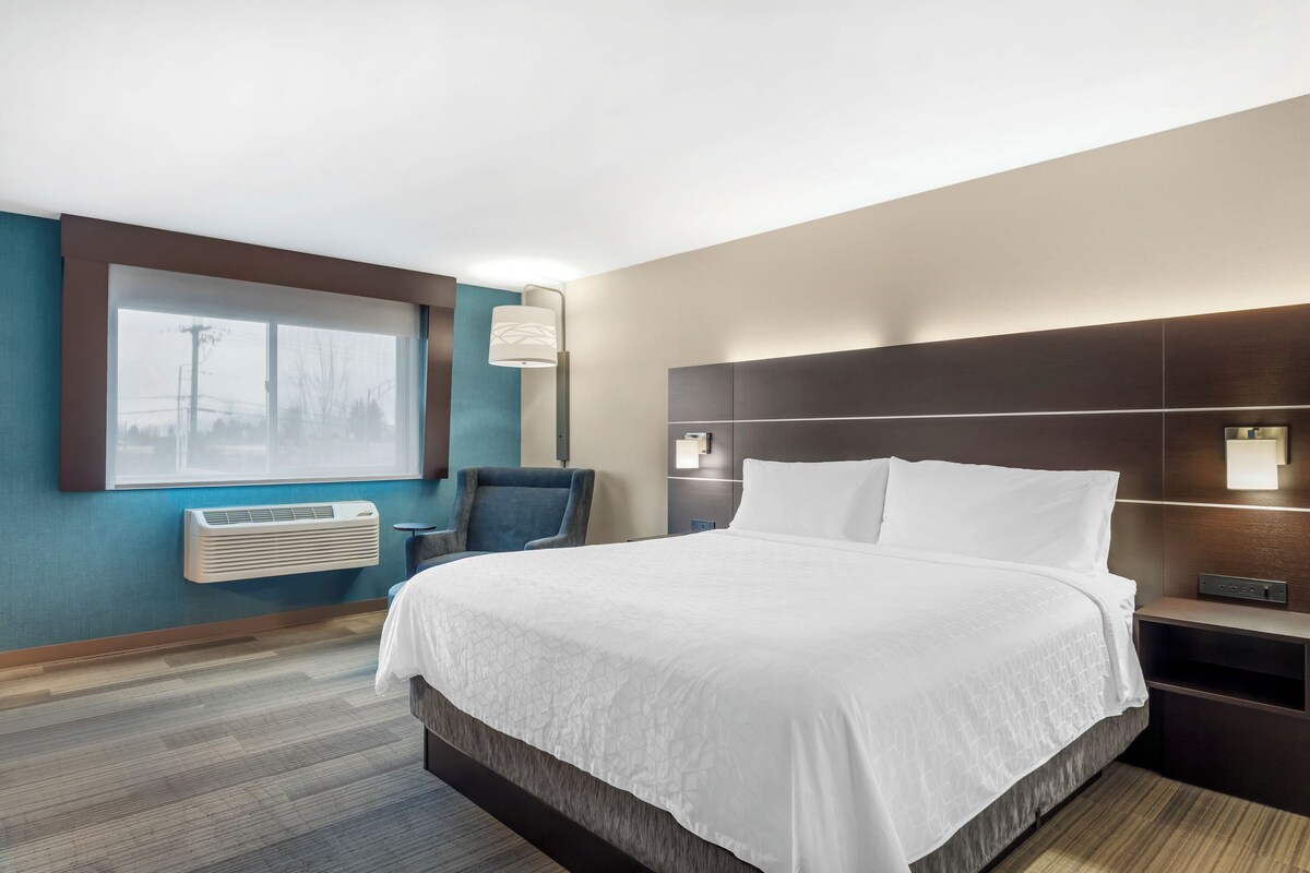 Une chambre d’hôtel avec un grand lit, une table de chevet, une chaise, une fenêtre donnant sur un paysage agréable et un climatiseur fixé au mur.