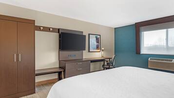 Ein Hotelzimmer mit Bett, Schreibtisch, Kleiderschrank, Flachbildfernseher und Klimaanlage.