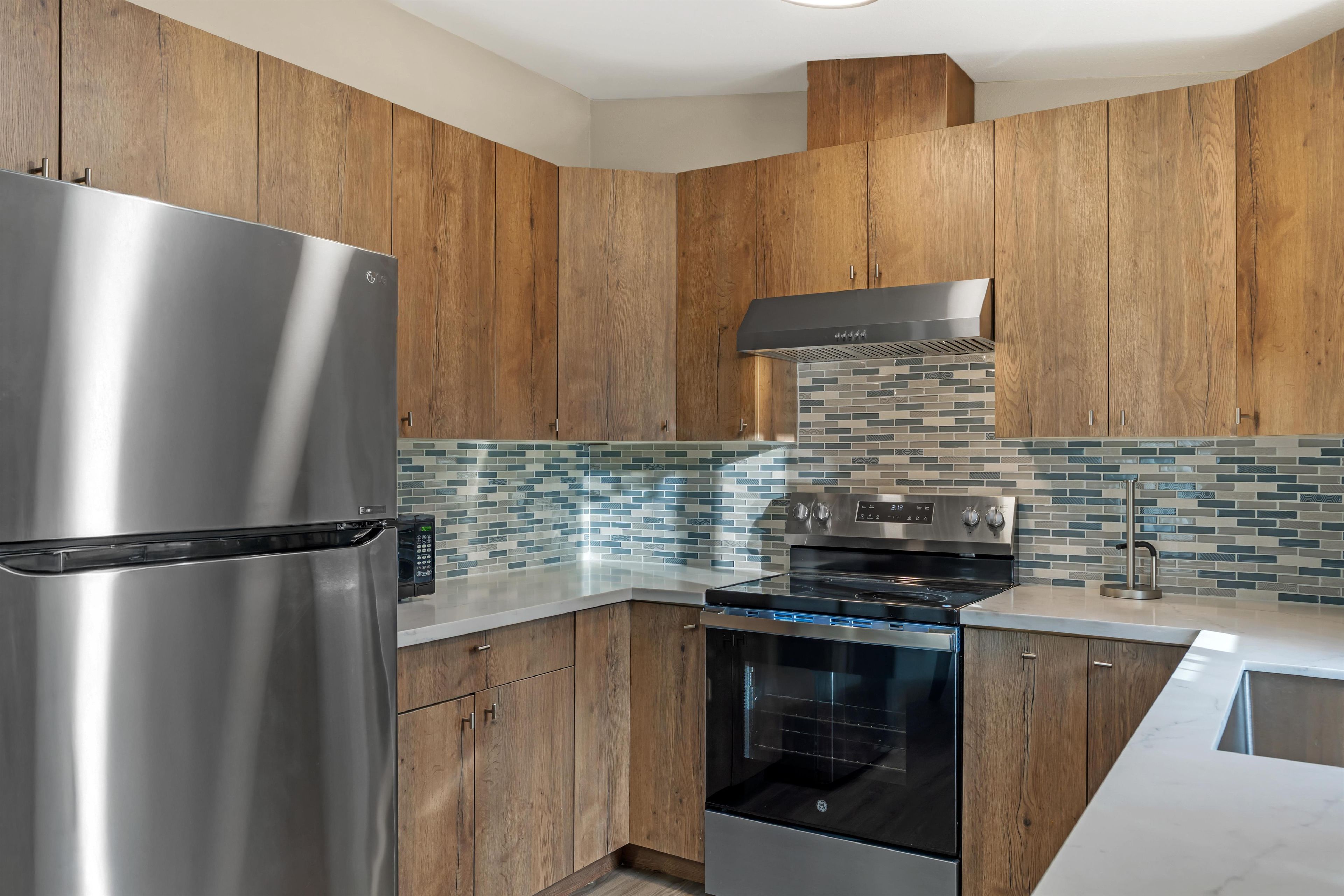 A modern kitchen with wooden cabinets, a stainless steel refrigerator, a built-in oven, and a microwave.
