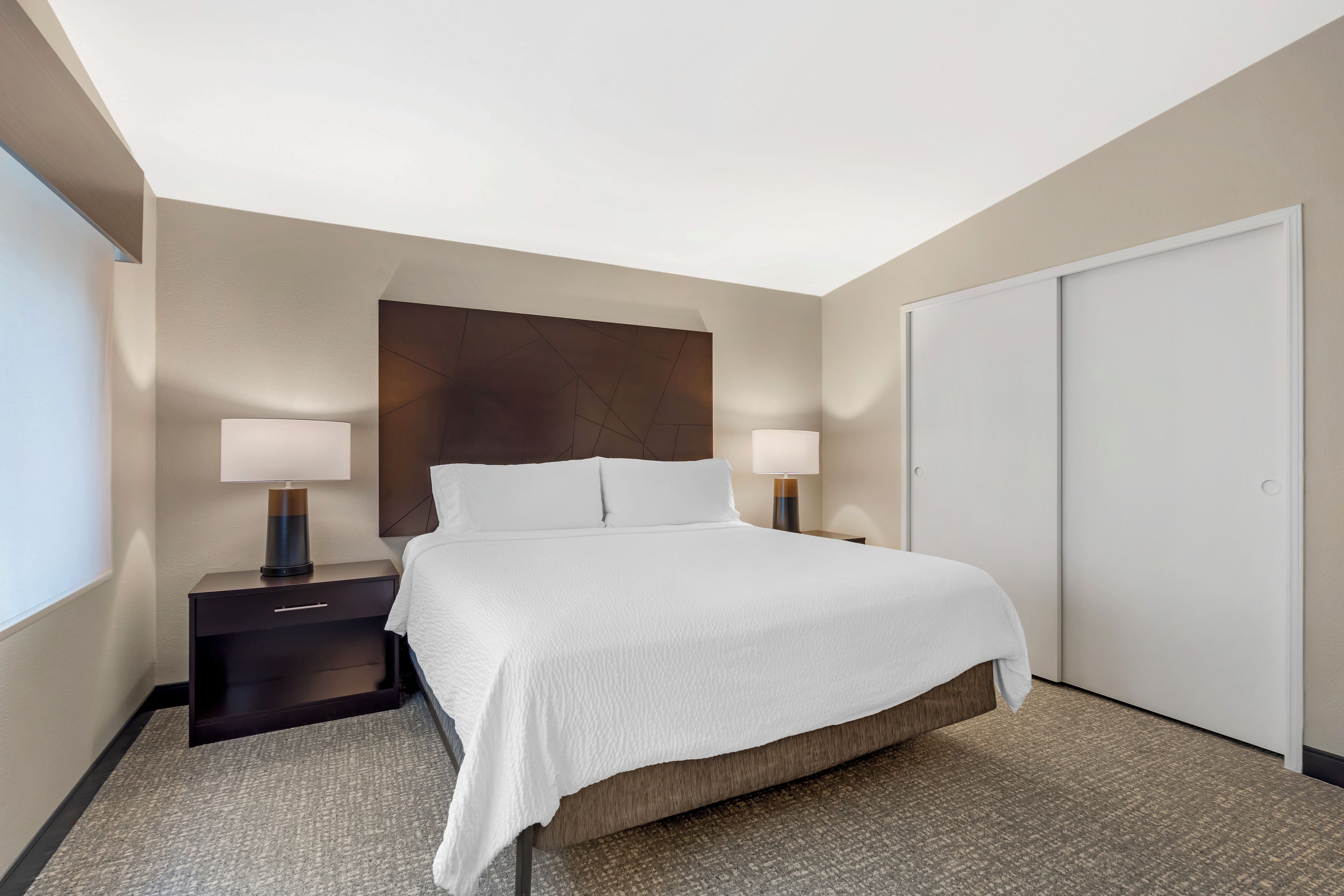 A hotel room with a large bed, two bedside tables with lamps, a wardrobe, and a carpeted floor.