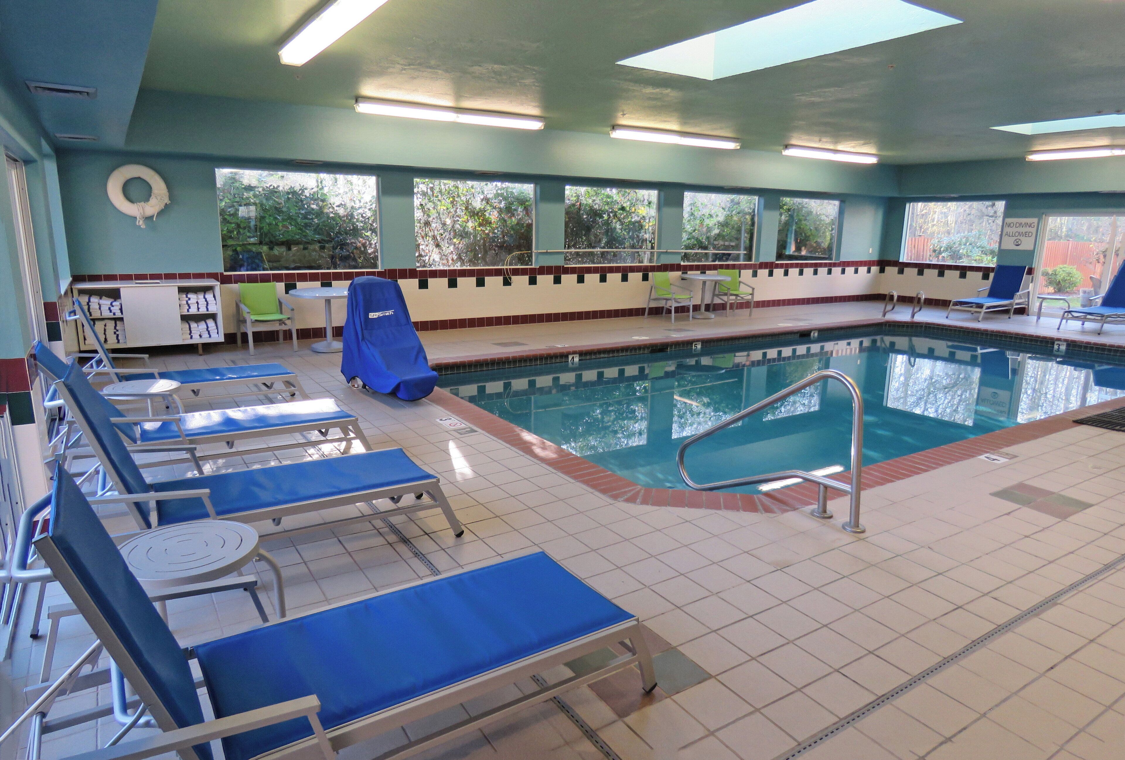 Une piscine intérieure dotée de chaises longues bleues, d’un plongeoir et d’un mur vitré.