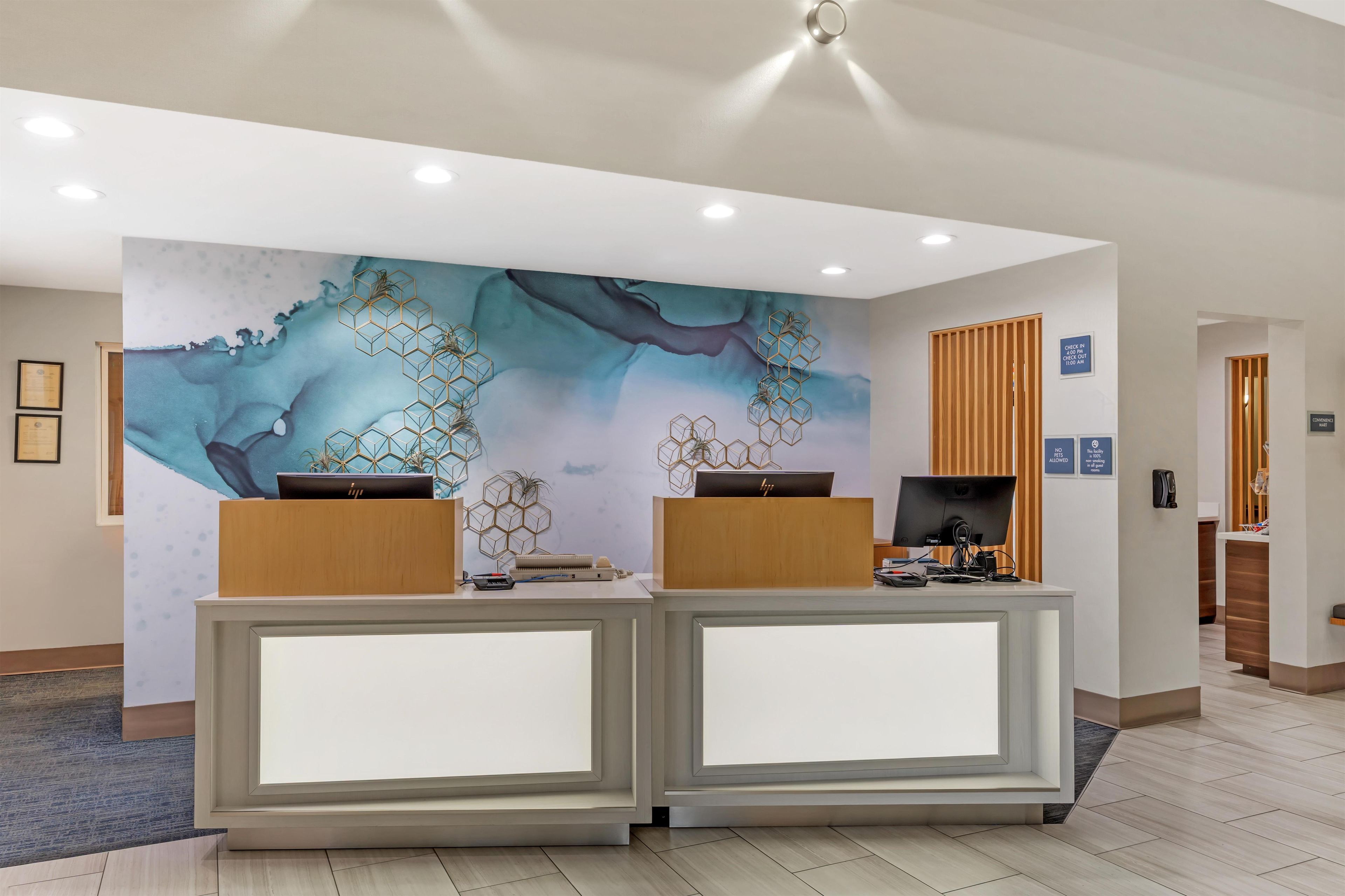 A reception desk with a modern design, a large abstract mural on the wall, and a check-in counter to the right.