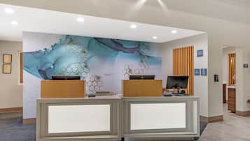A reception desk with a modern design, a large abstract mural on the wall, and a check-in counter to the right.