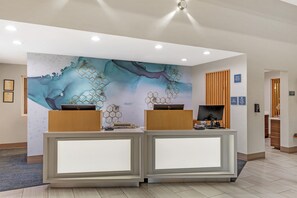 Un comptoir d’accueil au design moderne, une grande fresque murale abstraite et un comptoir d’enregistrement situé à droite.