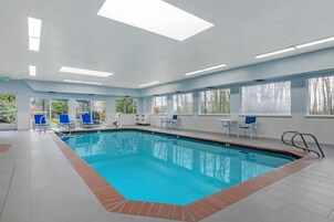 Piscina com água azul cristalina, rodeada por cadeiras e mesas azuis, com amplas janelas que dão vista para árvores.