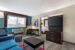 A modern hotel room with a large bed, a desk, a chair, a TV, and a sofa.