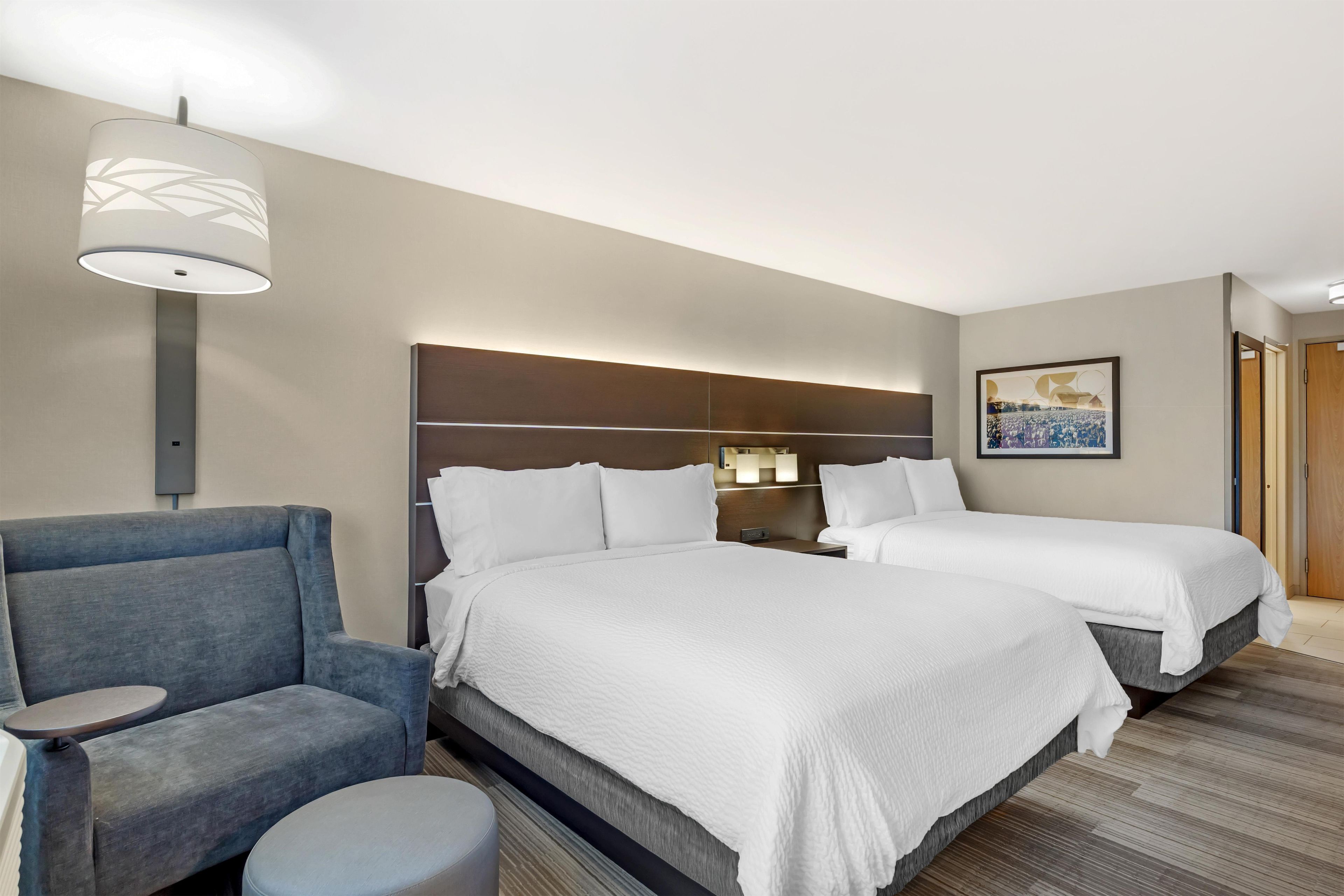 Habitación de hotel con dos camas, un sofá, una mesita y una lámpara de pared.
