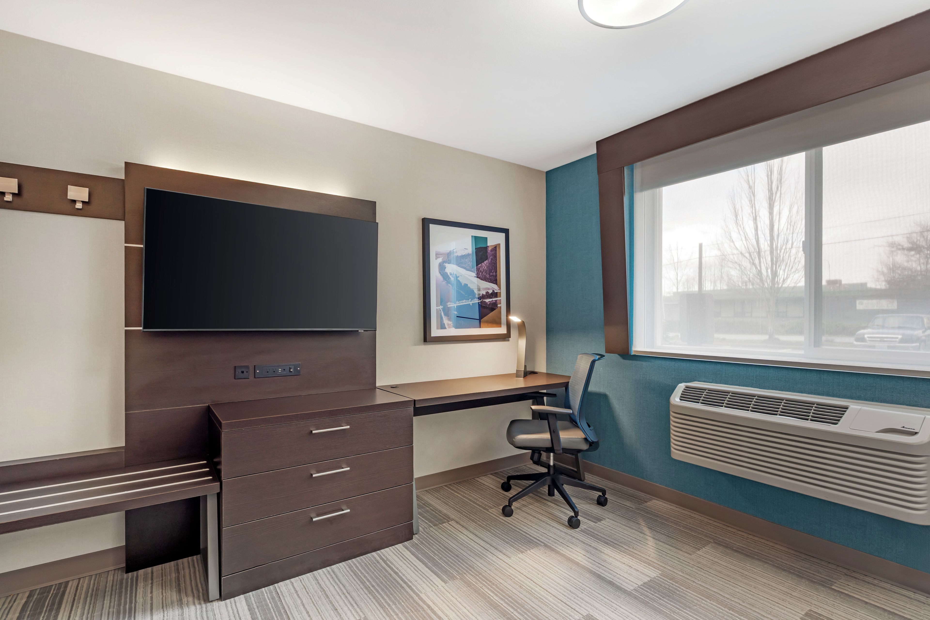 A modern office space with a desk, chair, built-in TV, and air conditioning unit.