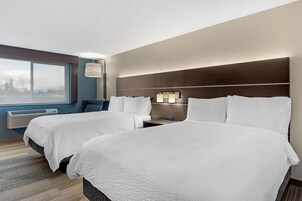 Habitación de hotel con dos camas, un ventanal grande, un equipo de aire acondicionado y una mesita de noche con lámpara.