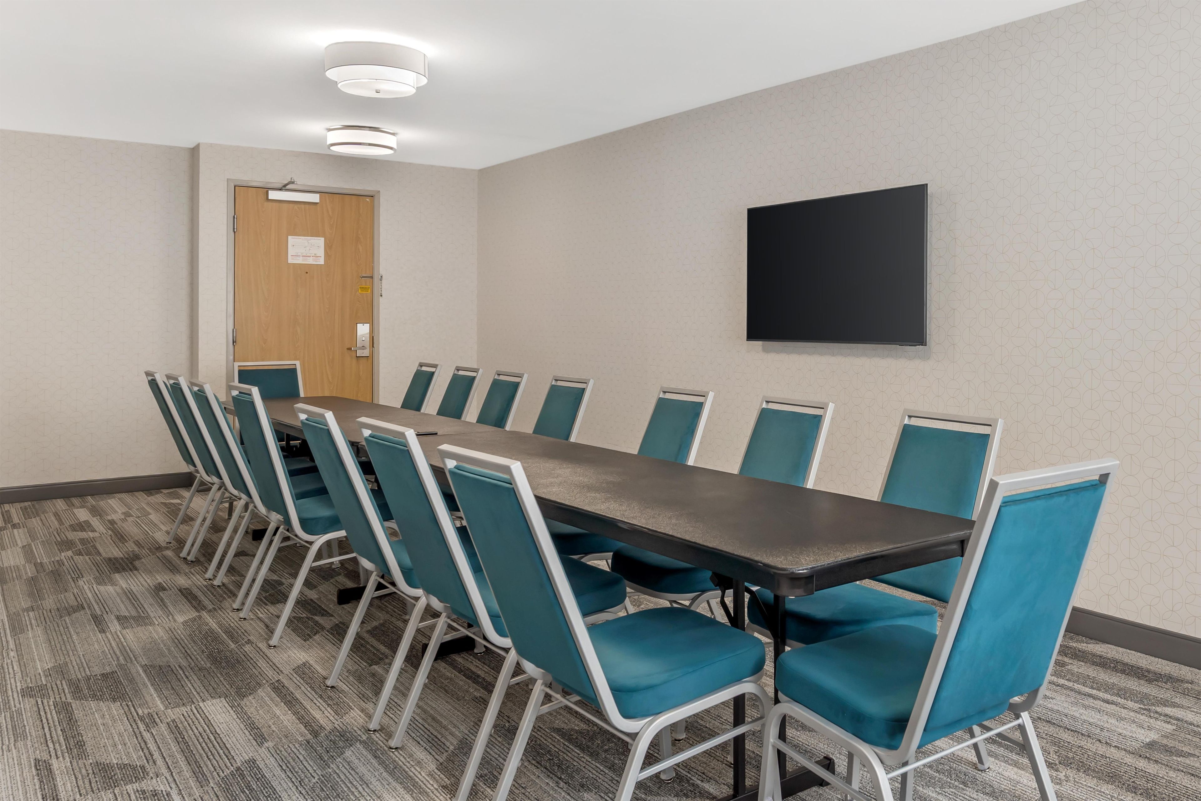A conference room with a long table and chairs, a door, and a flat-screen TV on the wall.