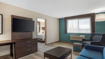 A hotel room with a flat-screen TV, a desk with drawers, a sofa, a coffee table, and a large window with a view.
