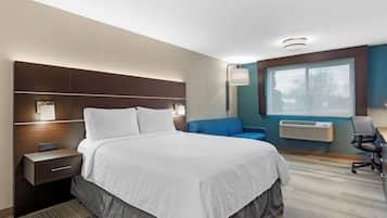 A hotel room with a large bed, bedside tables, a desk, a chair, a window, and an air conditioning unit.