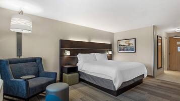 A hotel room with a bed, a chair, a bedside table, a lamp, and a picture on the wall.