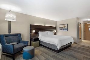 Habitación de hotel con cama, una silla, mesita de noche, lámpara y un cuadro en la pared.