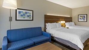 Ein Hotelzimmer mit einem blauen Sofa, einem Bett mit weißer Bettwäsche, einem Holzkopfende, einer Wandleuchte und einer gerahmten Farbpalette an der Wand.