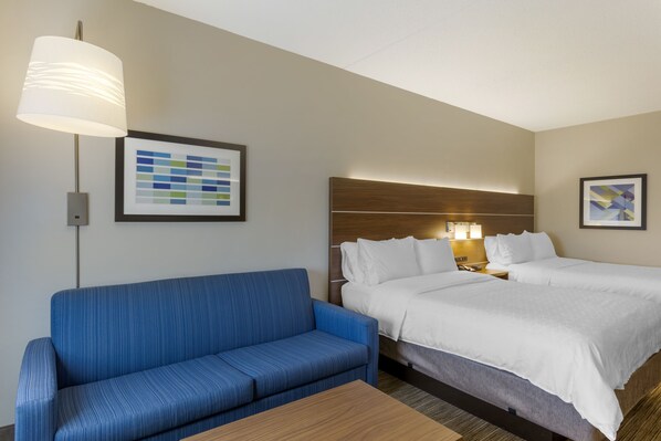 A hotel room with a blue sofa, a bed with white bedding, a wooden headboard, a wall-mounted lamp, and a framed color palette on the wall. - Holiday Inn Express Hotel & Suites Harrison by IHG (Harrison)