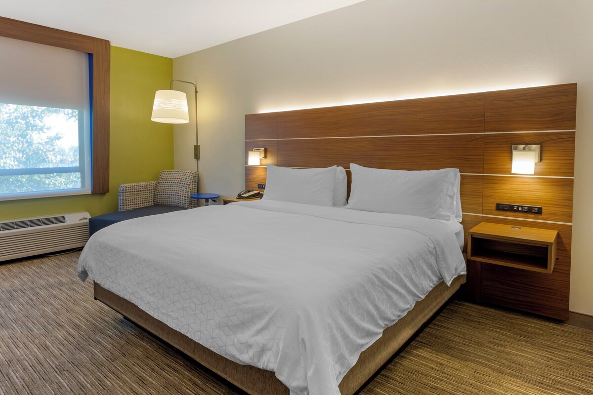 A hotel room with a large bed, a bedside table with a lamp, a chair, and a wall-mounted phone.