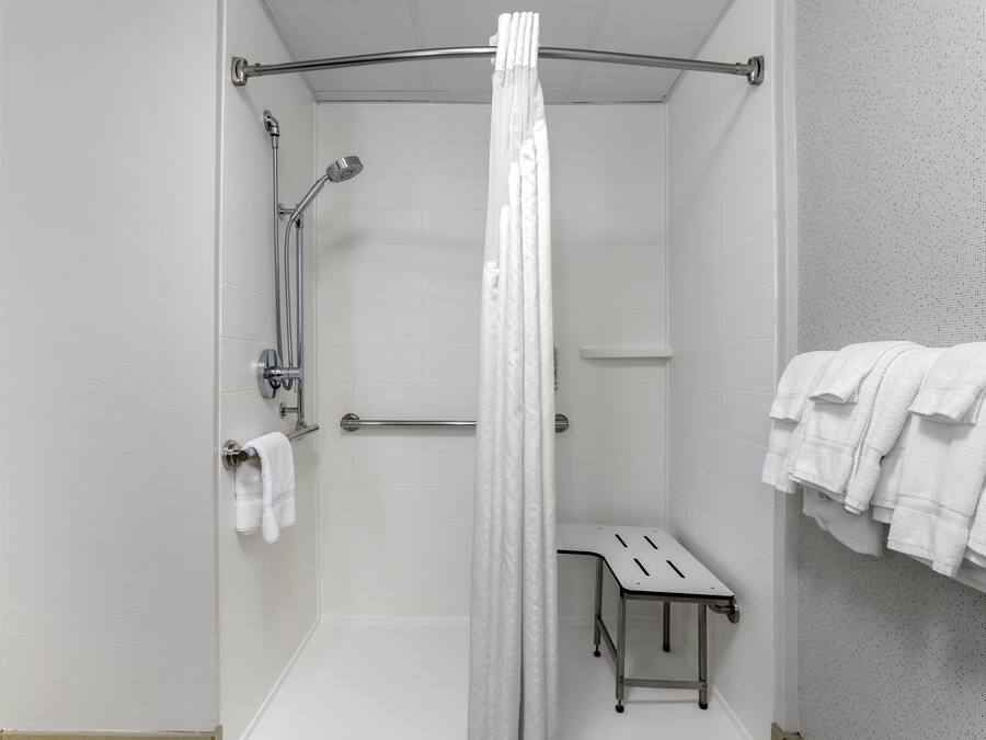 Et bruseområde med glasdør, et håndklædetørrestativ med håndklæder og et lille bord.