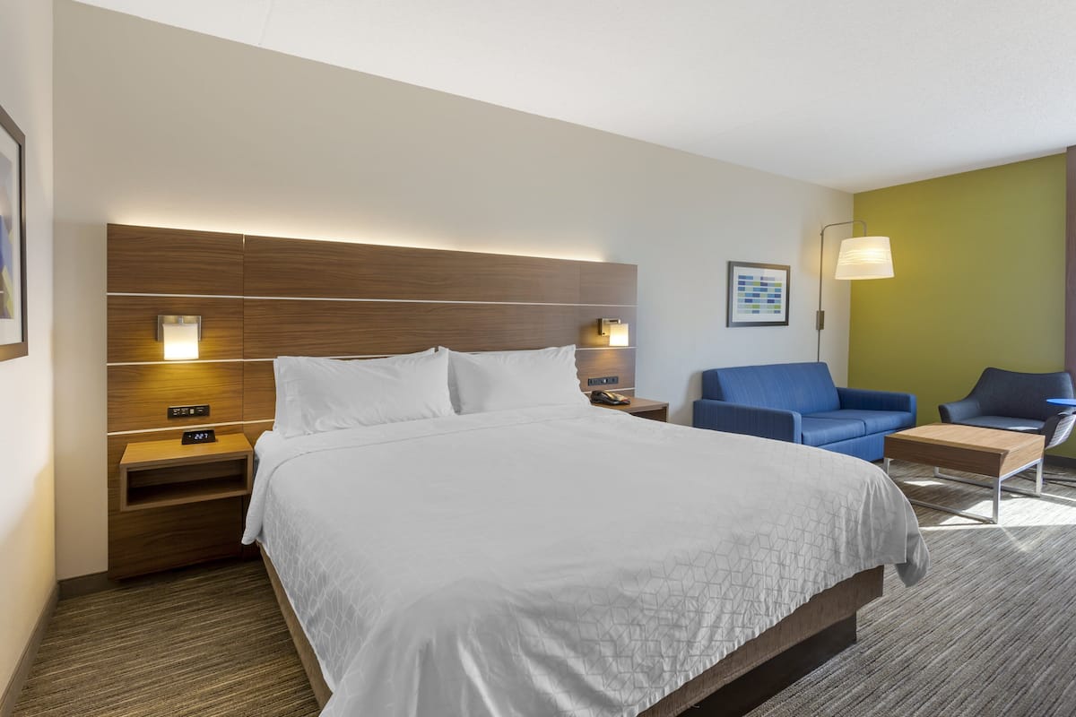 A hotel room with a large bed, a nightstand, a blue sofa, a chair, and a wall-mounted lamp.