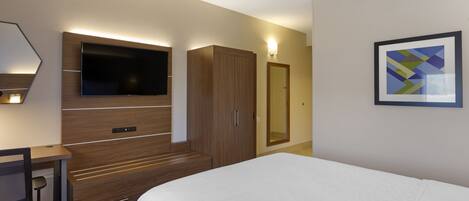 Habitació d'hotel amb llit, escriptori, televisió, armari i un quadre al mur.