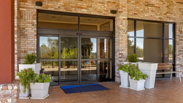 A building entrance with glass doors, potted plants, and a bench. - Holiday Inn Express Hotel & Suites Harrison by IHG (Harrison)