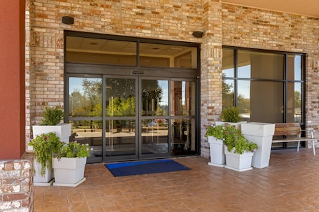 A building entrance with glass doors, potted plants, and a bench.