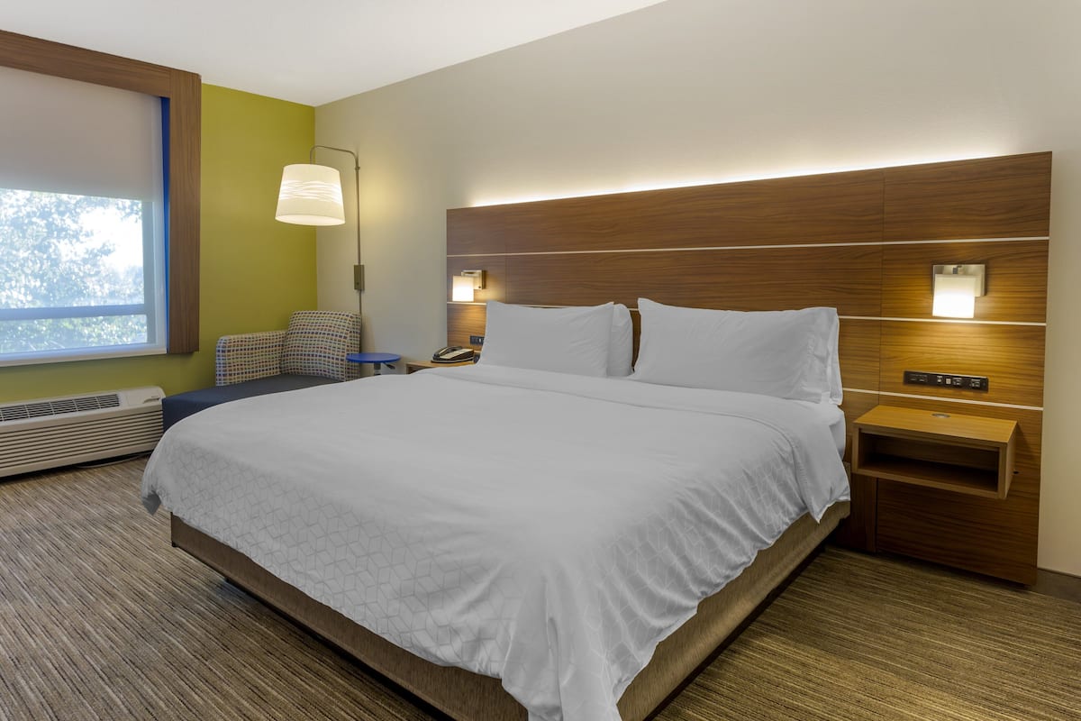 A hotel room with a large bed, a bedside table with a lamp, a chair, and a wall-mounted phone.