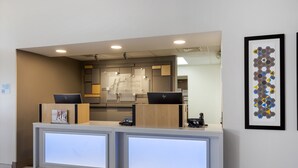 A hotel reception desk with two computer stations, a reception area, and a framed artwork on the wall.