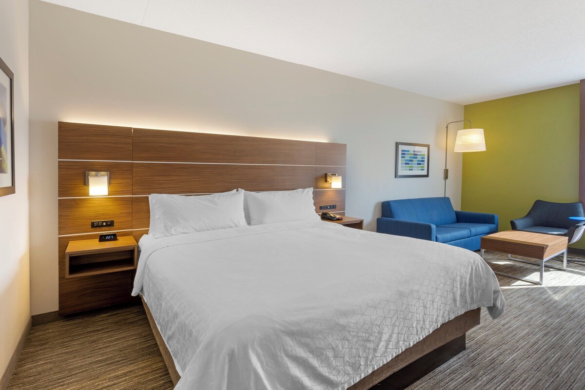 A hotel room with a large bed, a nightstand, a blue sofa, a chair, and a wall-mounted lamp.