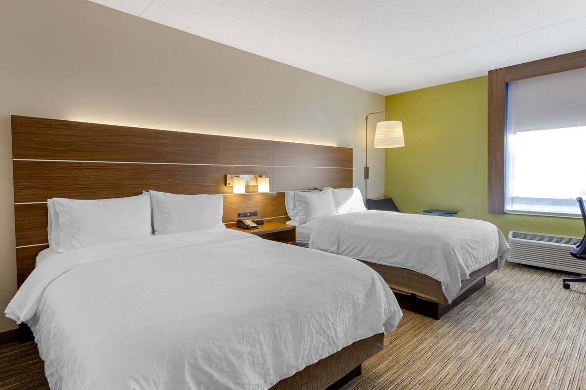 A hotel room with two beds, a wooden headboard, bedside lamps, a nightstand, and a large window.