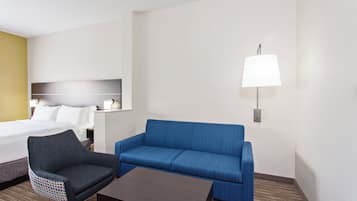 Une chambre d’hôtel avec un lit, un canapé bleu, un petit fauteuil, une table basse et une lampe fixée au mur.
