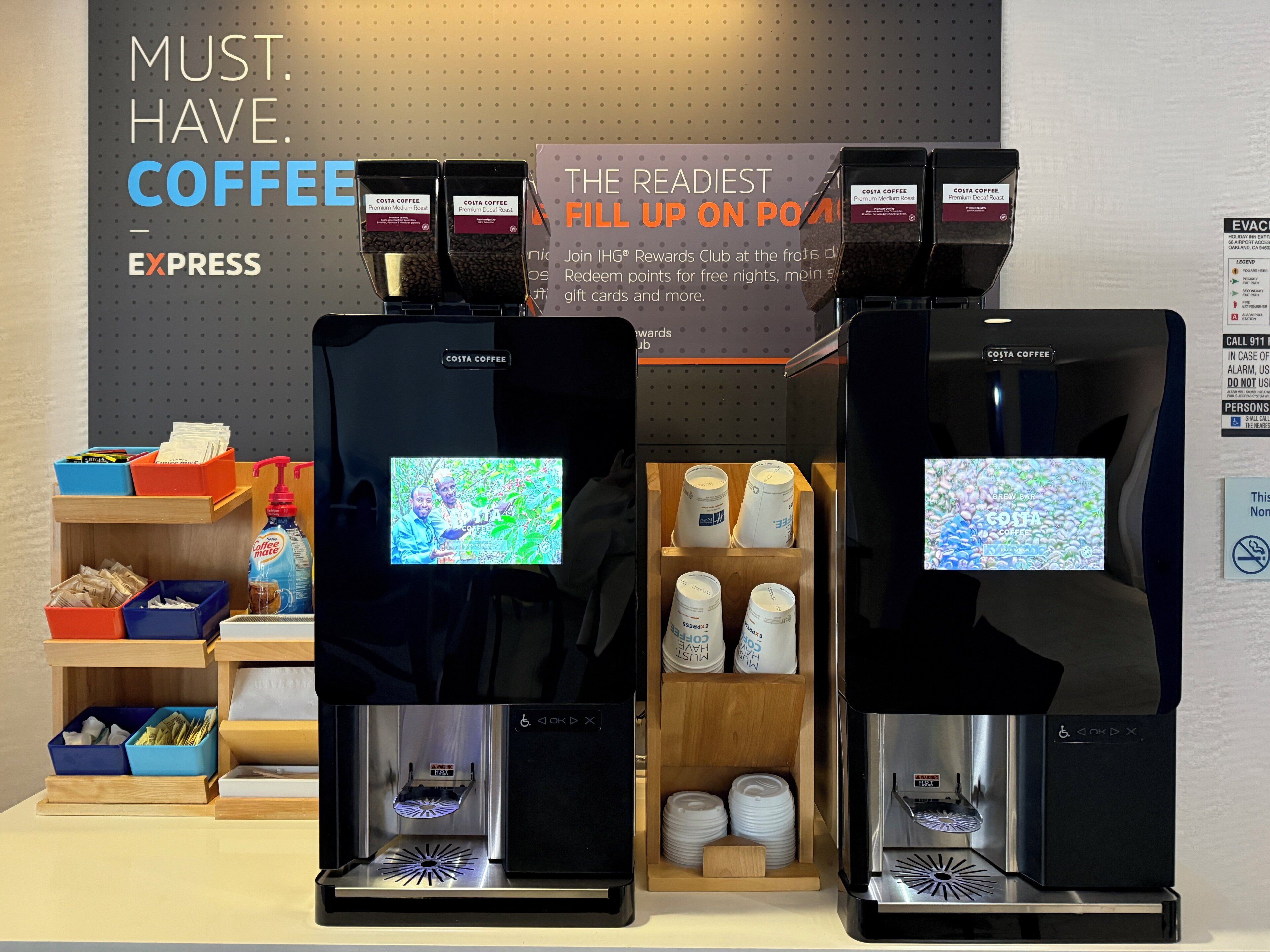 Two coffee machines with digital displays, a signboard, and storage containers with coffee cups.