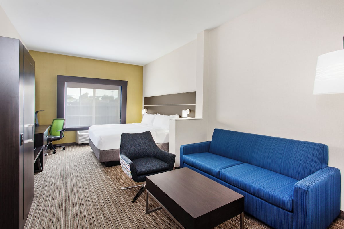 Habitación de hotel con una cama, un sofá azul, una mesita, un sillón verde y un escritorio con una computadora.