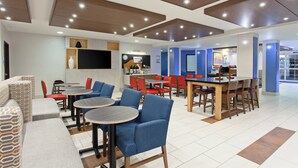 Un restaurante moderno con mesas redondas y sillas azules, un televisor de pantalla plana y una zona de barra.