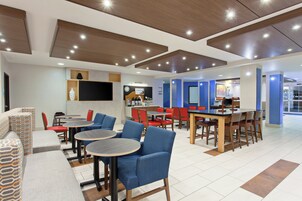 Un restaurante moderno con mesas redondas y sillas azules, un televisor de pantalla plana y una zona de barra.
