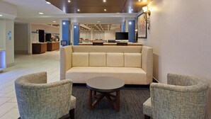 Un hall con un sofá, dos sillones, una mesita de centro, un televisor y un mostrador de recepción.