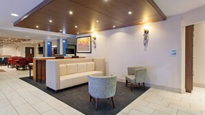 Un vestíbulo de hotel con una recepción, un sofá, sillas y un área de comedor con mesas y sillas.