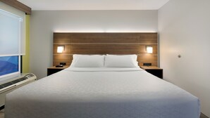 A hotel room with a large bed, two bedside tables, a wall-mounted TV, and a ceiling-mounted air conditioning unit.