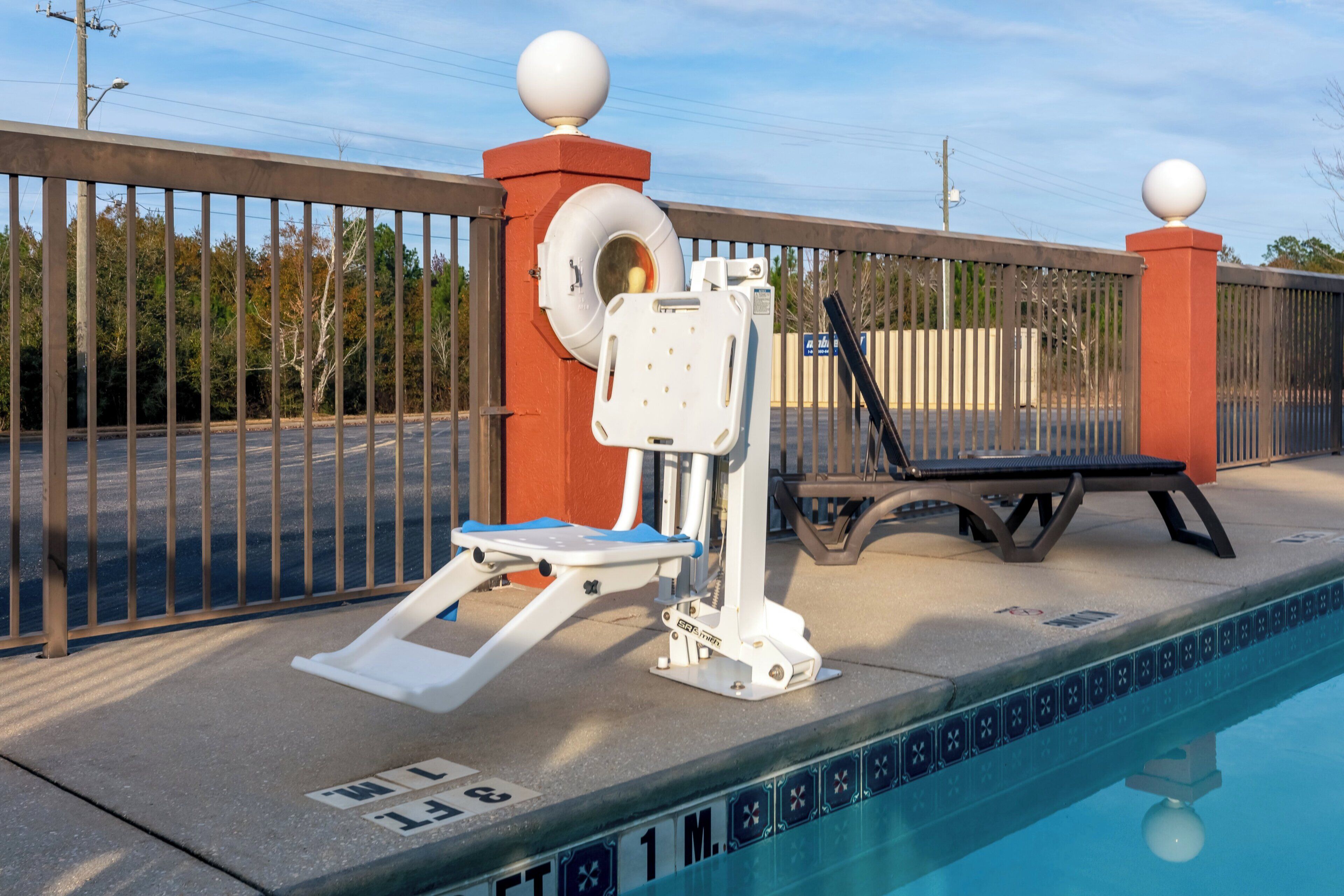 A swimming pool with a diving board, a lounge chair, and a fence with decorative elements.