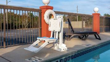 A swimming pool with a diving board, a lounge chair, and a fence with decorative elements.