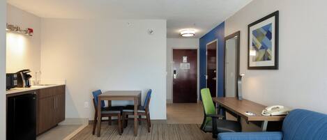 A hotel room with a kitchenette, a dining area with a table and chairs, a sofa, and a desk with a phone.