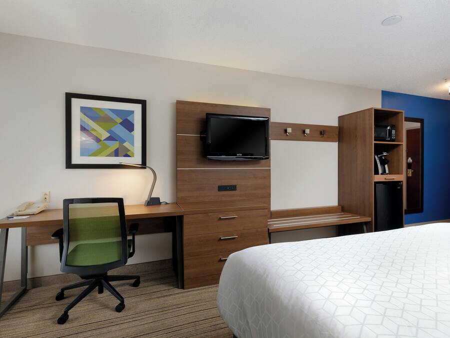 A hotel room with a bed, desk, chair, television, and a small cabinet.