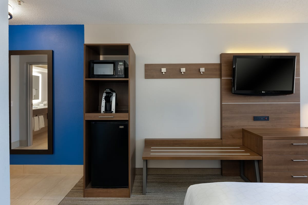 A hotel room with a bed, a desk with a flat-screen TV, a microwave, a coffee maker, and a mini-fridge.