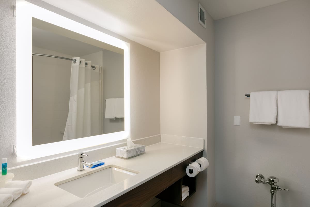A bathroom with a large mirror, a sink, a shower, and a towel rack.
