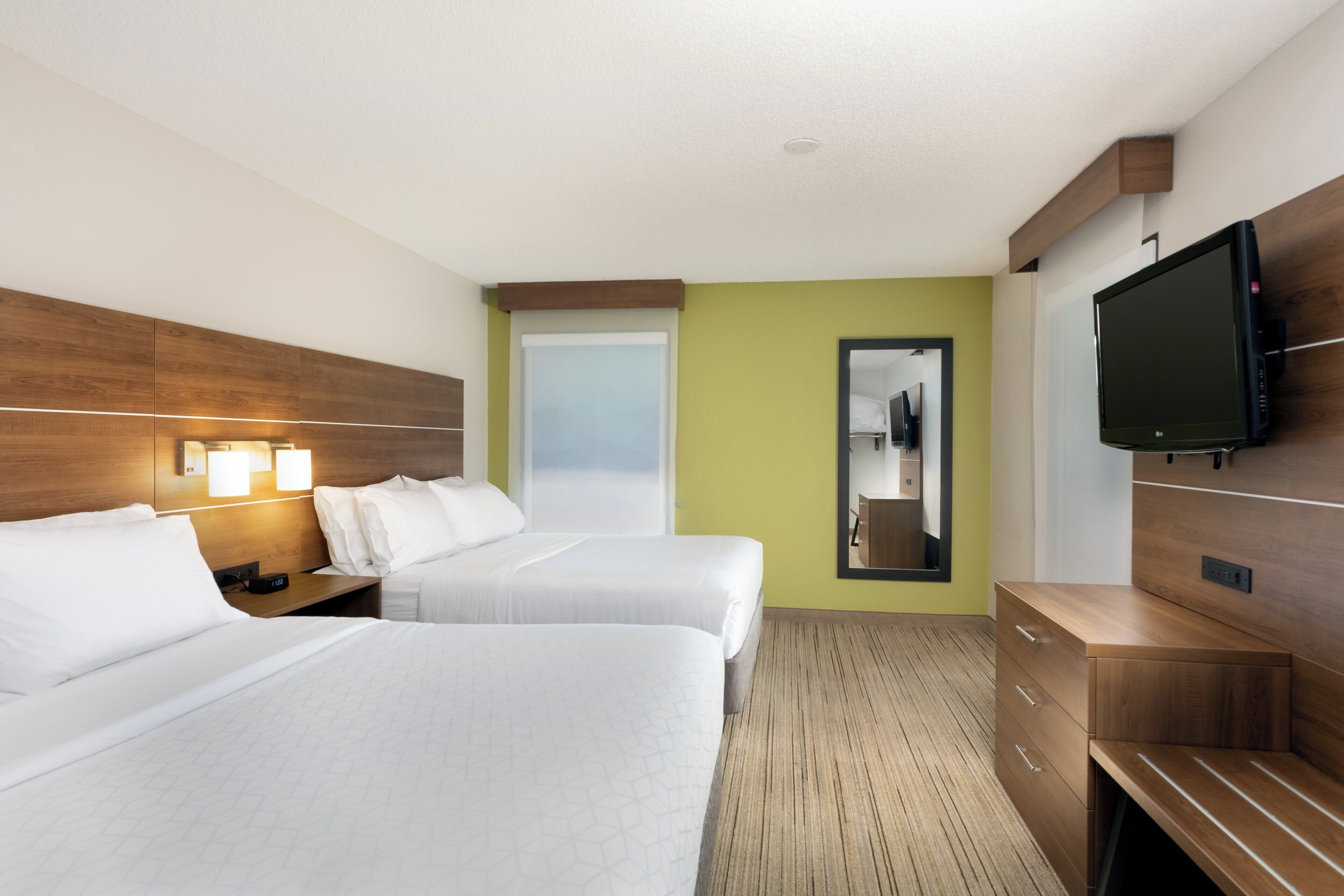 A hotel room with two beds, a TV, a mirror, and a wooden dresser.