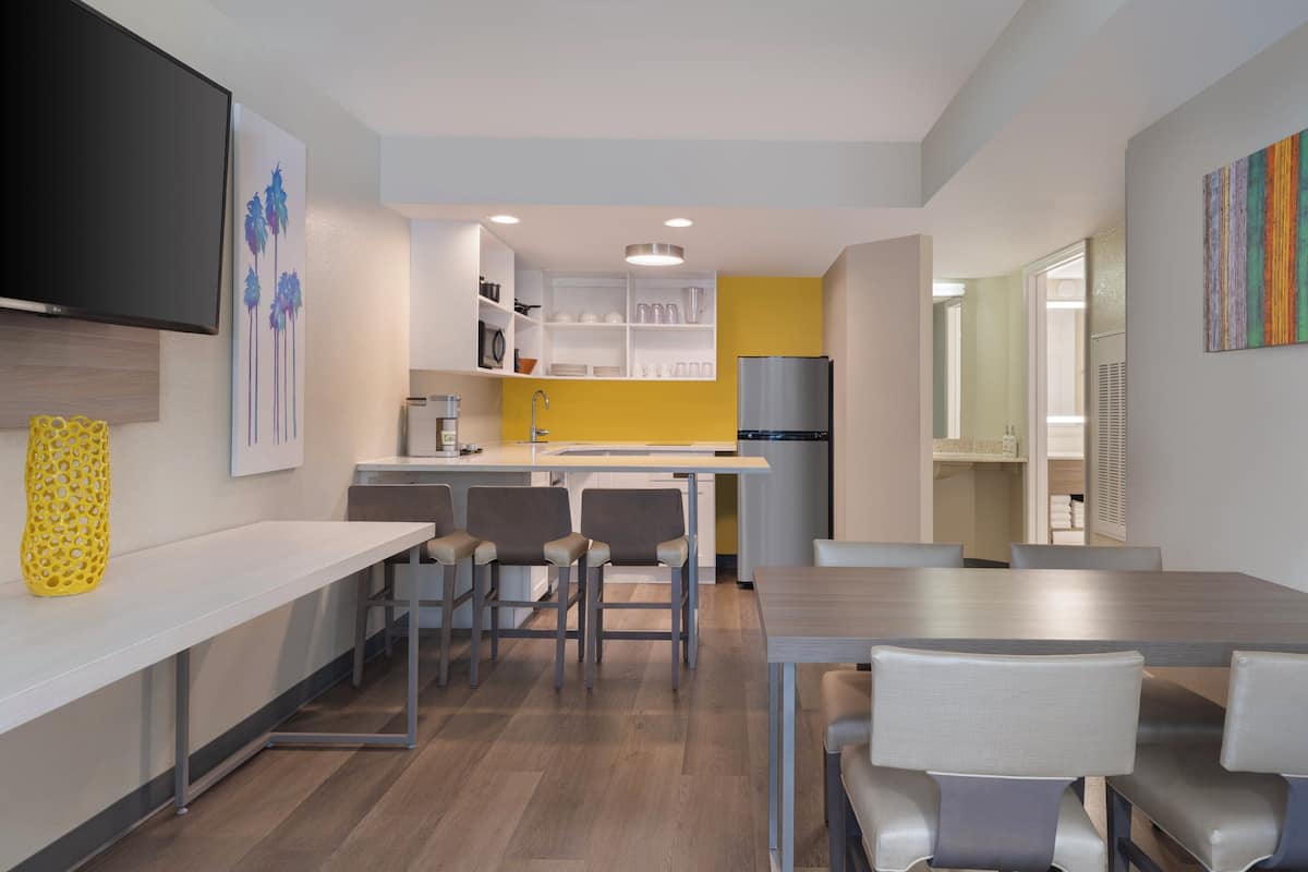 A modern kitchen with white cabinetry, a yellow accent wall, and a stainless steel refrigerator.