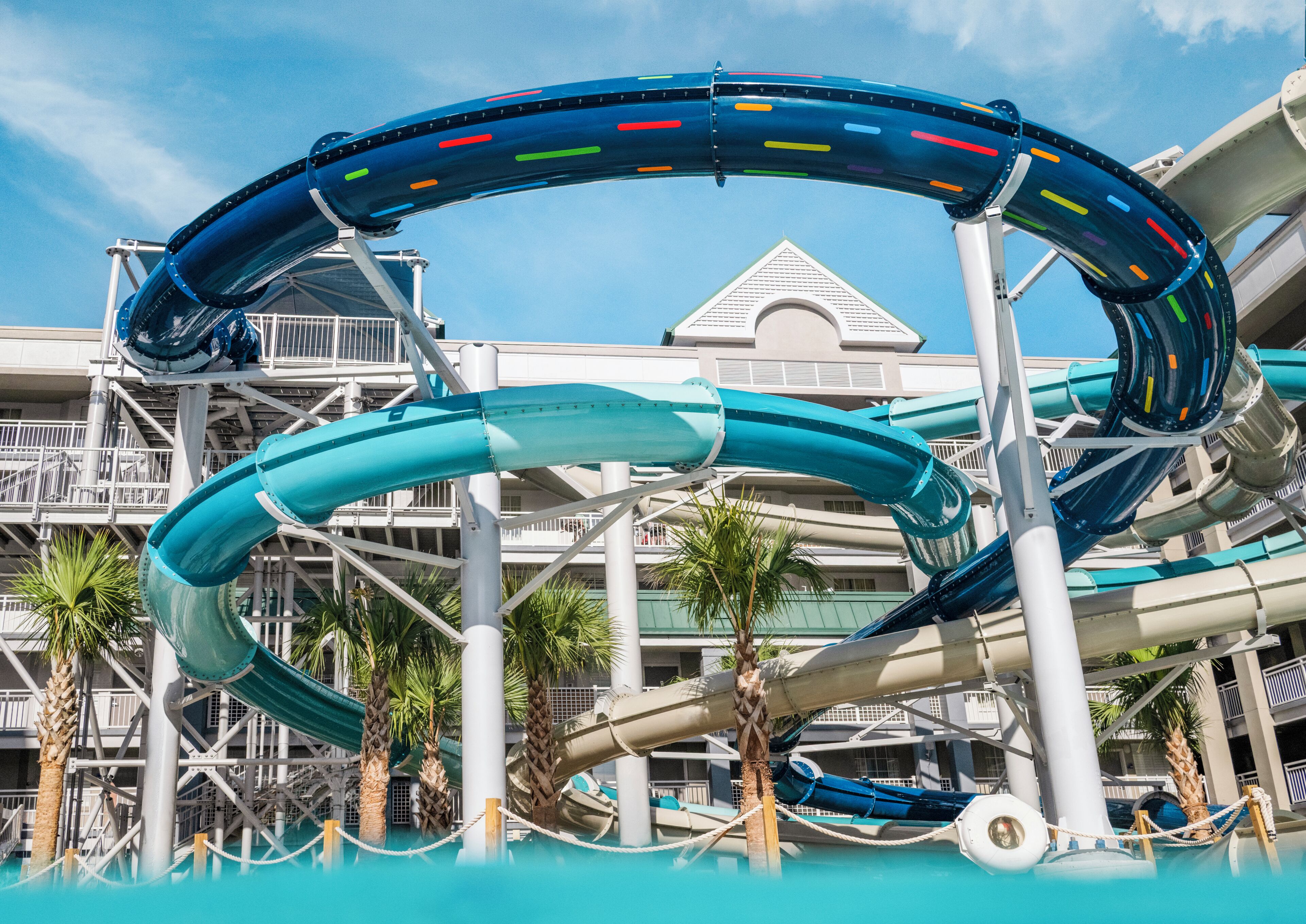 A water park with a large water slide, palm trees, and a building with balconies.